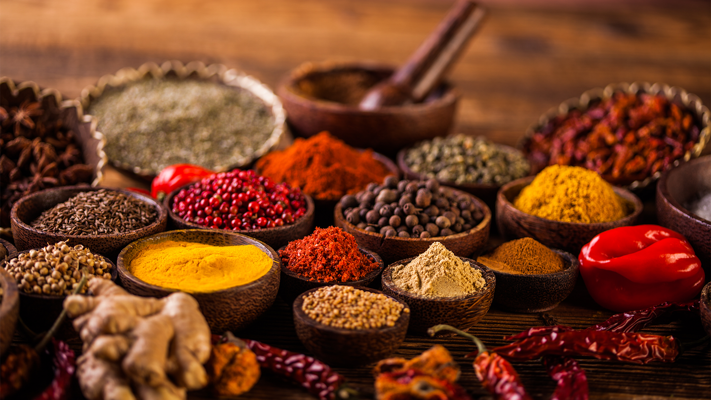 A group of colorful spices on a wooden table with a mortar and pestle.
