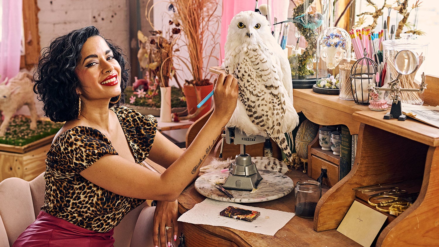 Divya Anantharaman sits at desk, works on replica snowy owl mount, with other taxidermied animals and materials in background