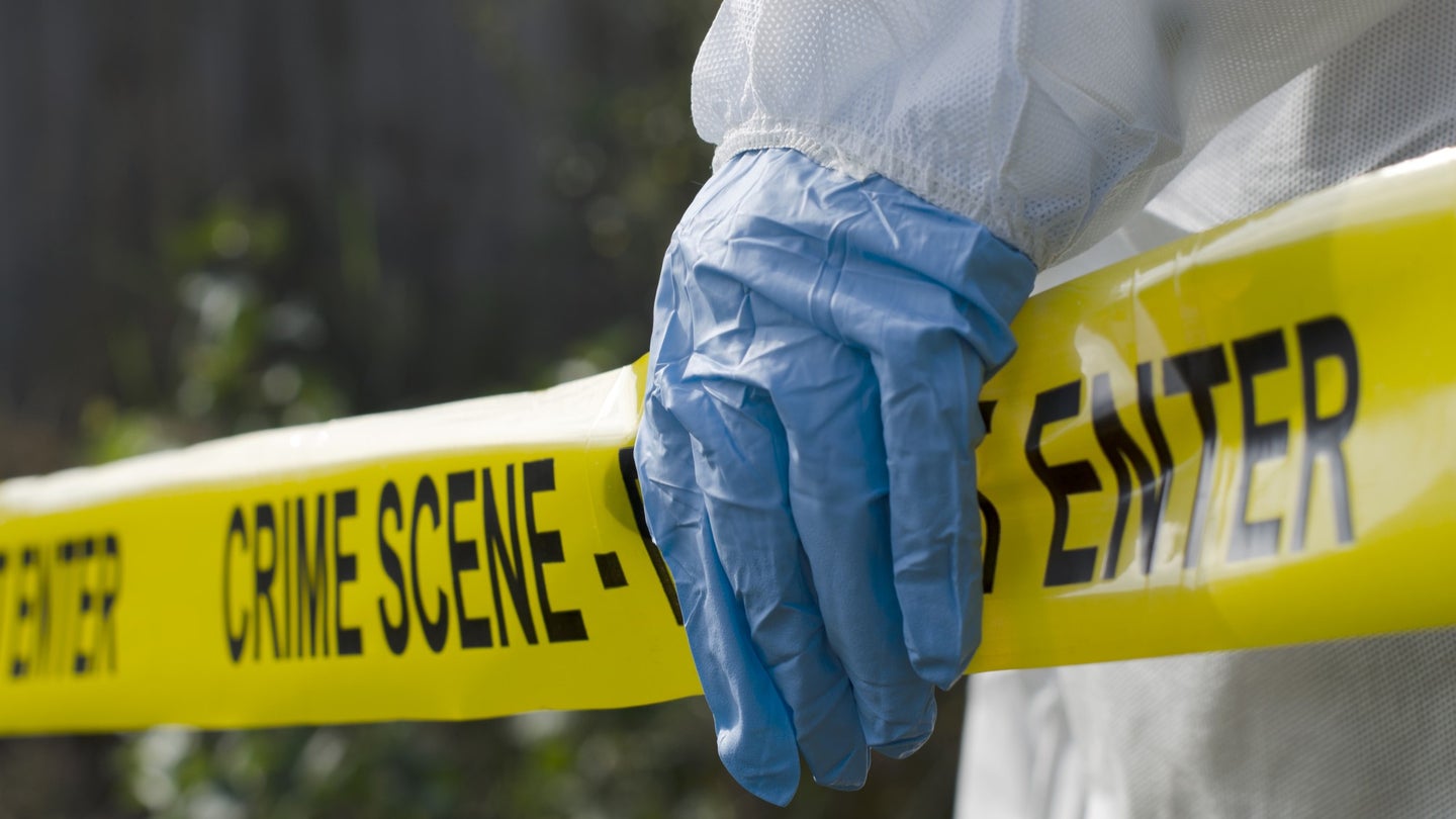 A gloved hand holds police tape in a crime scene investigation.