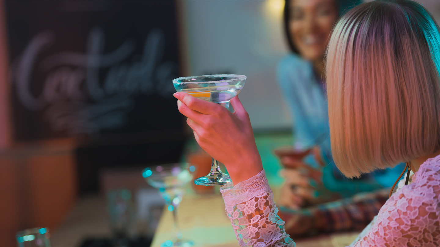 A woman holds an alcoholic drink in a bar.