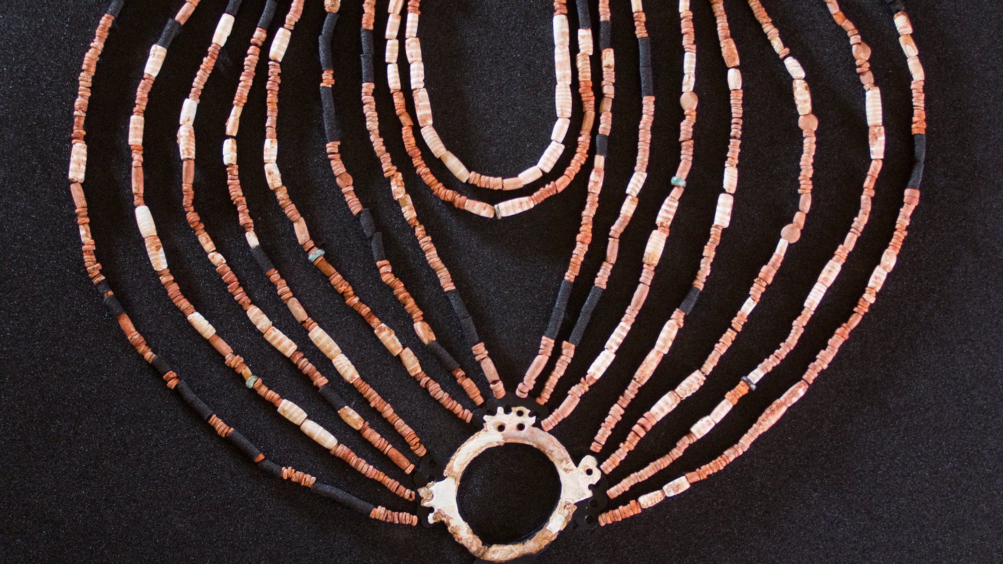 The physical reconstruction of the necklace found in the Neolithic village of Ba’ja in Jordan. It has about 16 strands of beads that meet together in a circle with a gemstone in it and three other strands on top.
