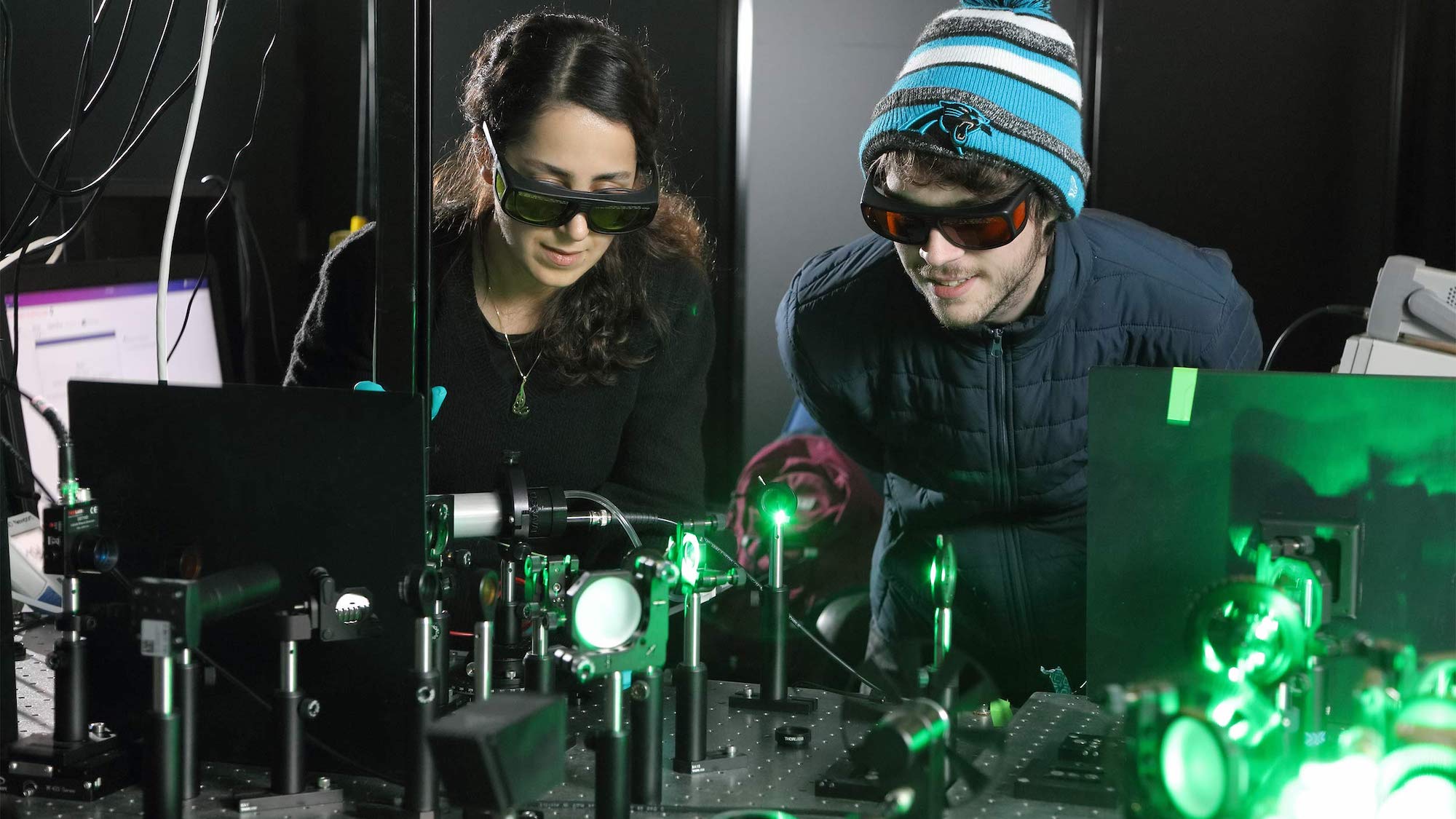 Two researchers look at green plasma ray in lab setting