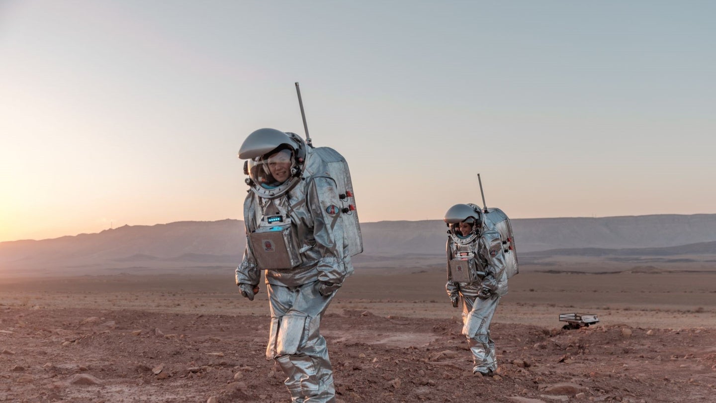 Two astronauts walking in spacesuits in a desert