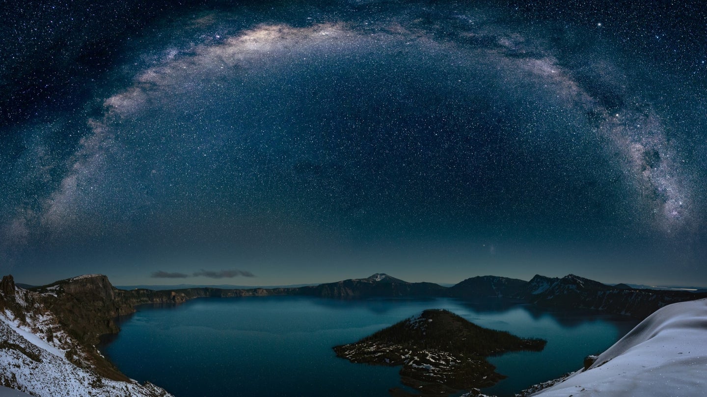 Stars form a half-circle above a mountain lake.