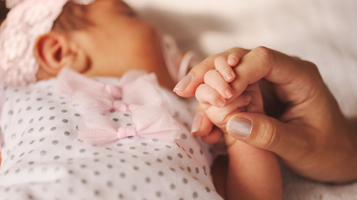 A mother holds a hand of a tiny newborn baby. Postpartum depression is a leading cause of maternal mortality.