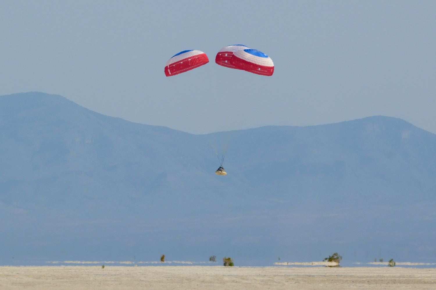 A parachute slows a Boeing space capsule above the New Mexico desert.
