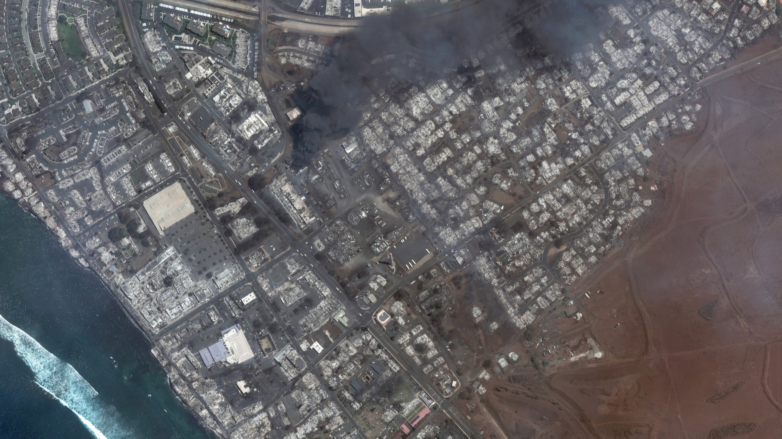 Maxar satellite imagery on August 9, 2023 showing total destruction of the Lahaina square and outlets after the Lahaina Wildfire, with one building still actively burning.