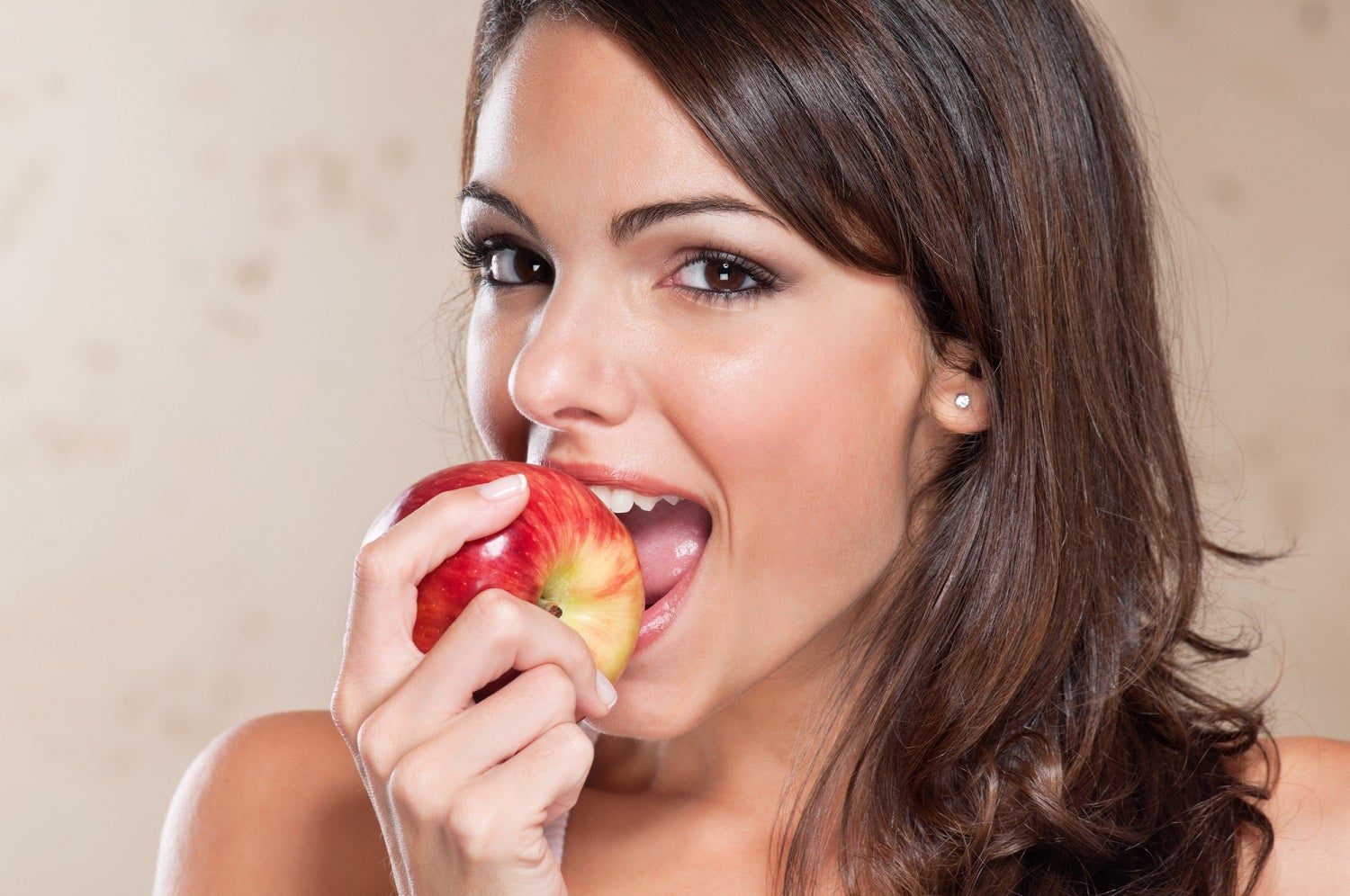 Person with long brown hair and white skin eating ripe red and yellow apple
