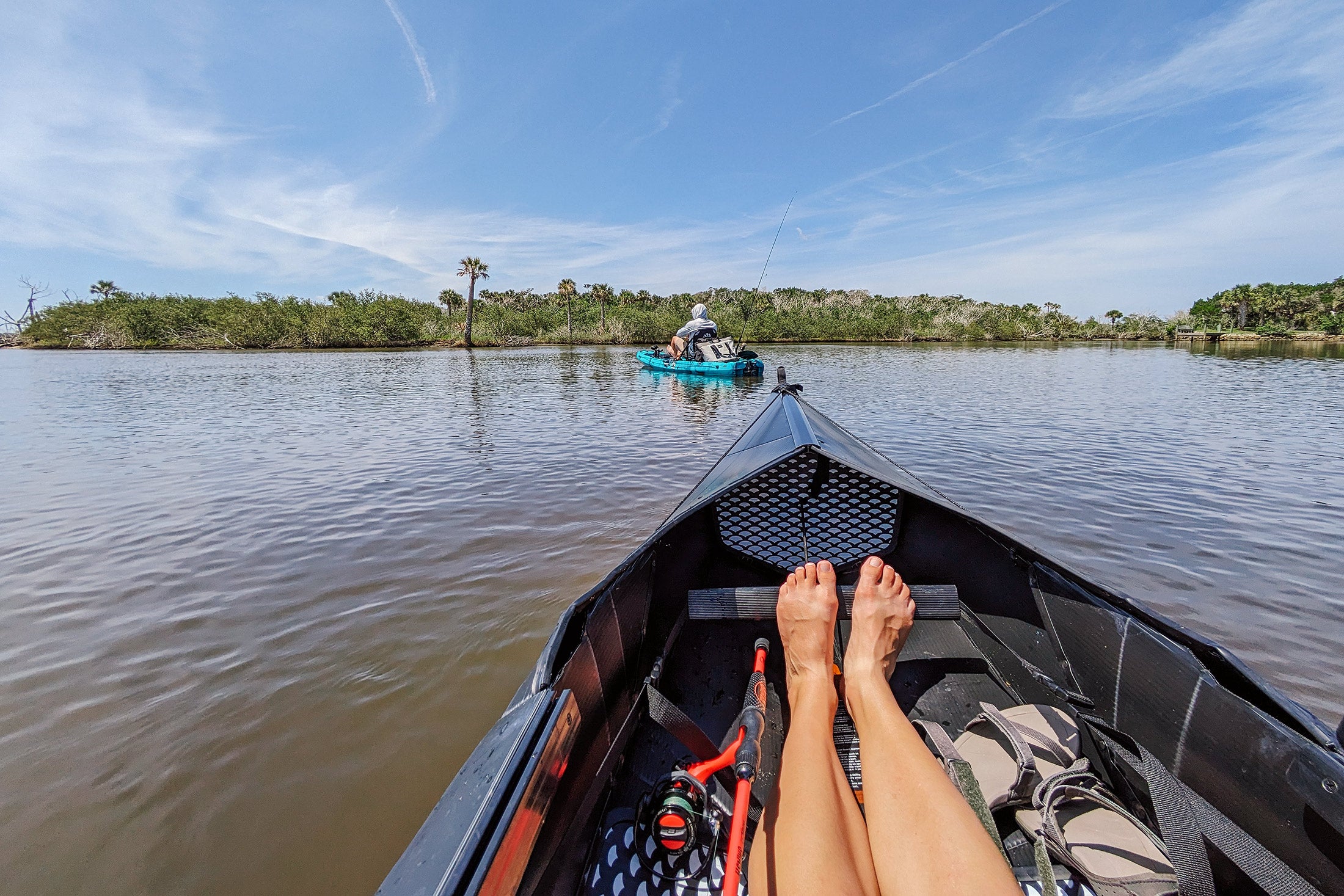 Legs stretched out in the Oru Kayak with another kayak in front on a river.