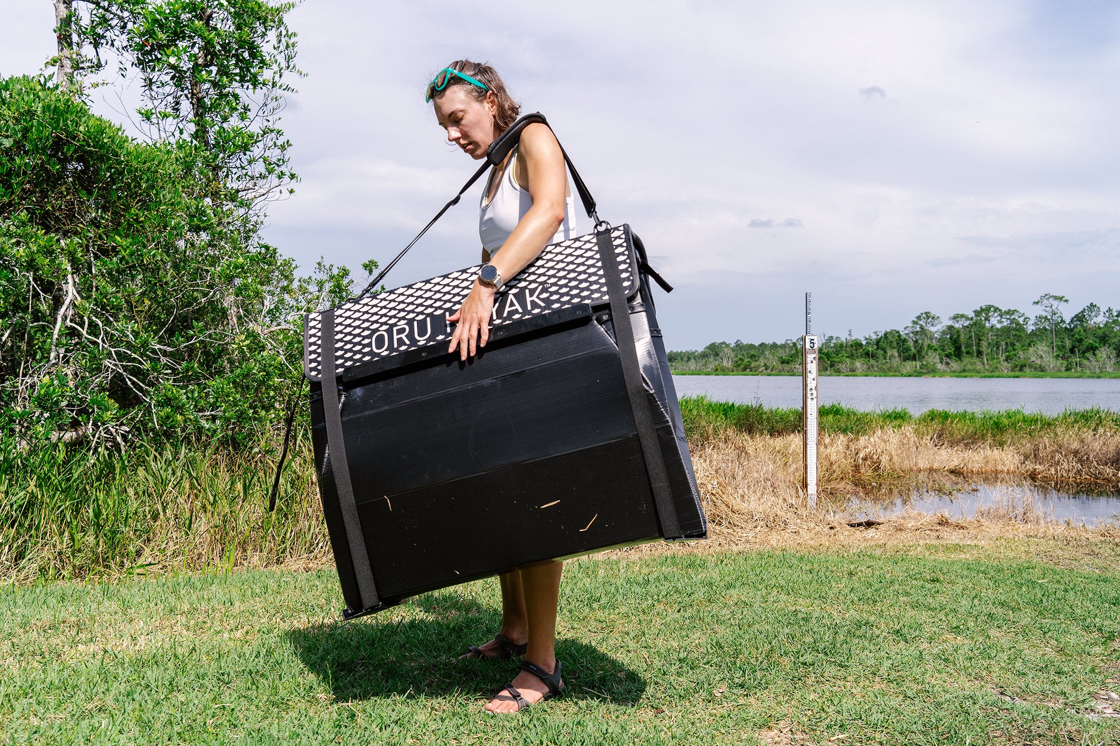 The Oru Beach LT Sport folded down and carried by a woman on a shoreline. 