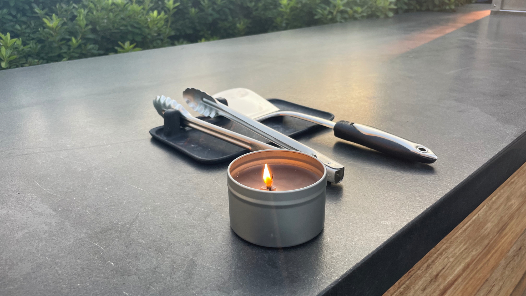 A DIY citronella candle in a small metal candle tin on a black surface outside.