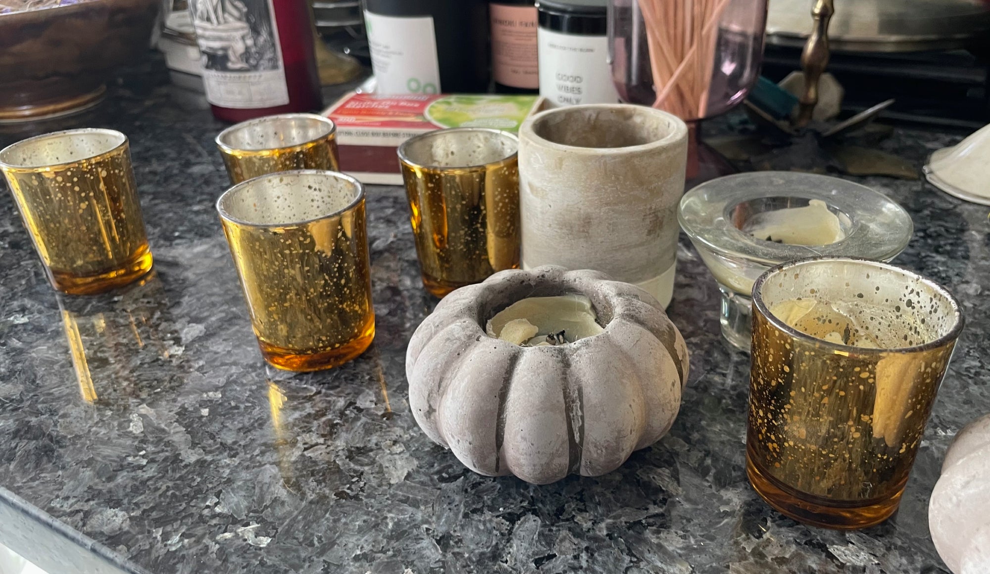 Several old candles in candle jars on a marble countertop, ready to be melted and made into new candles.