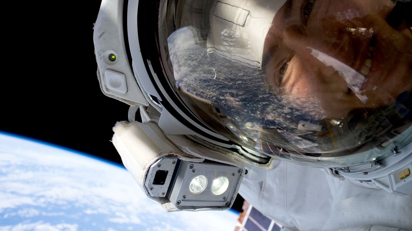 A close-up astronaut outside the ISS above a blue slice of Earth.