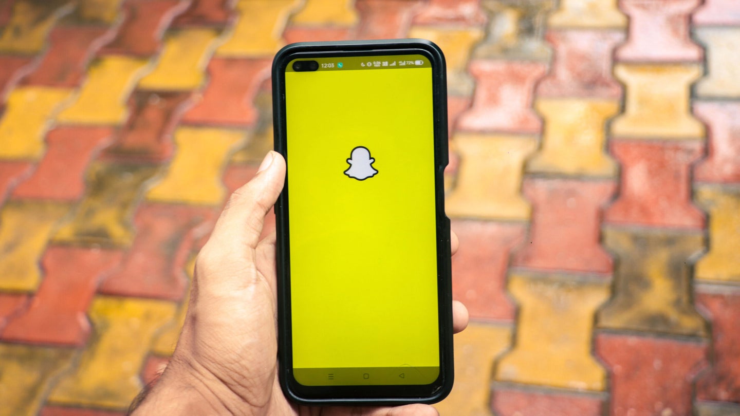 A person holding a cell phone with the Snapchat app open on it.