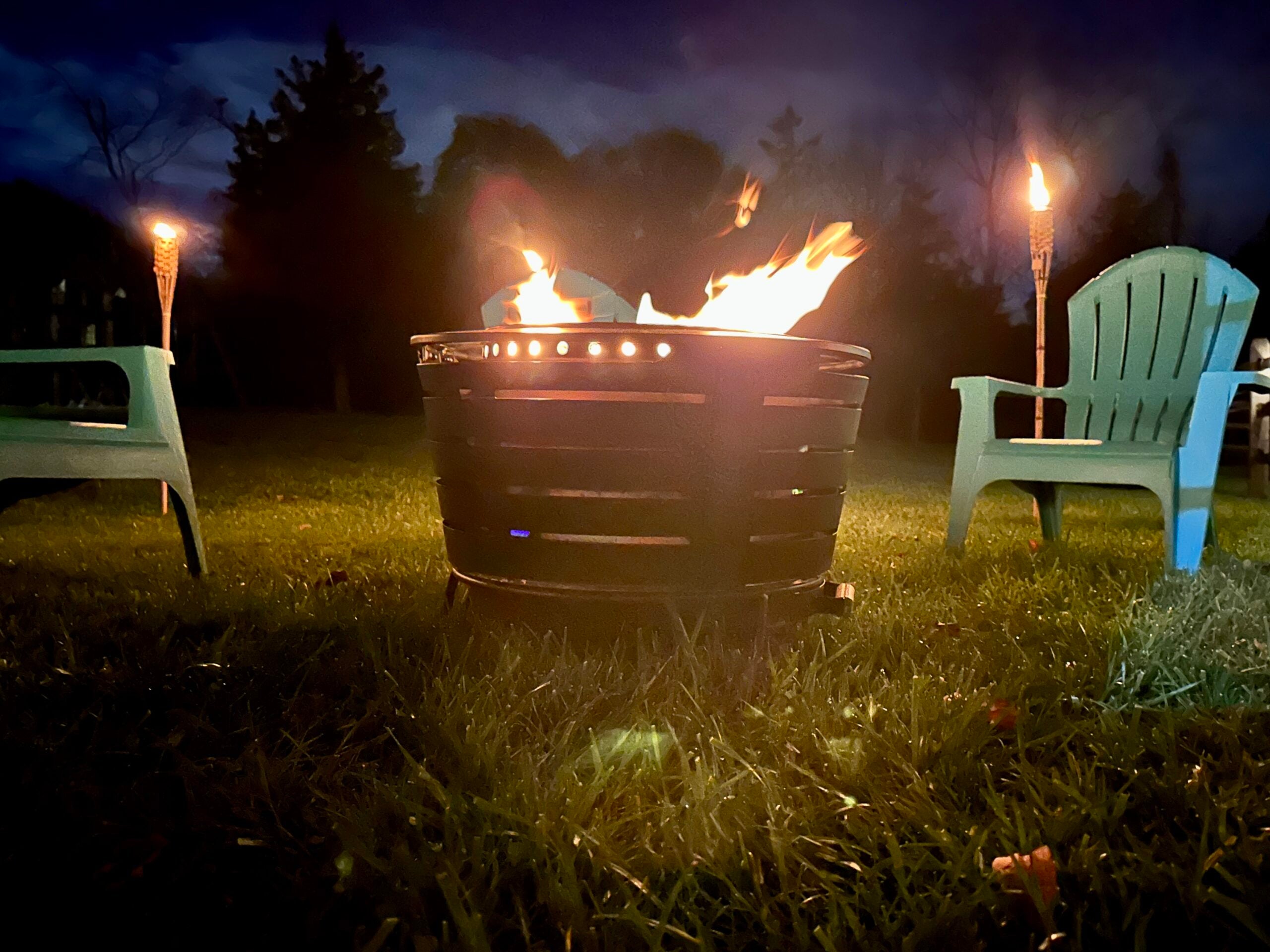 Tiki smokeless fire pit with a fire going at night surrounded by torches and chairs