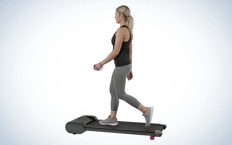 A woman in a black tank top and gray leggings walking on a compact treadmill.