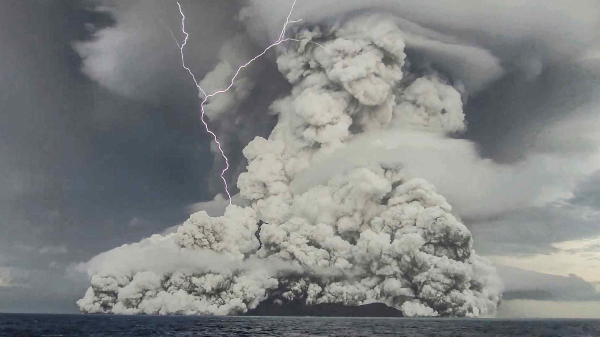 An eruption emerges from the ocean in a cloud of ash and a lightning strike.