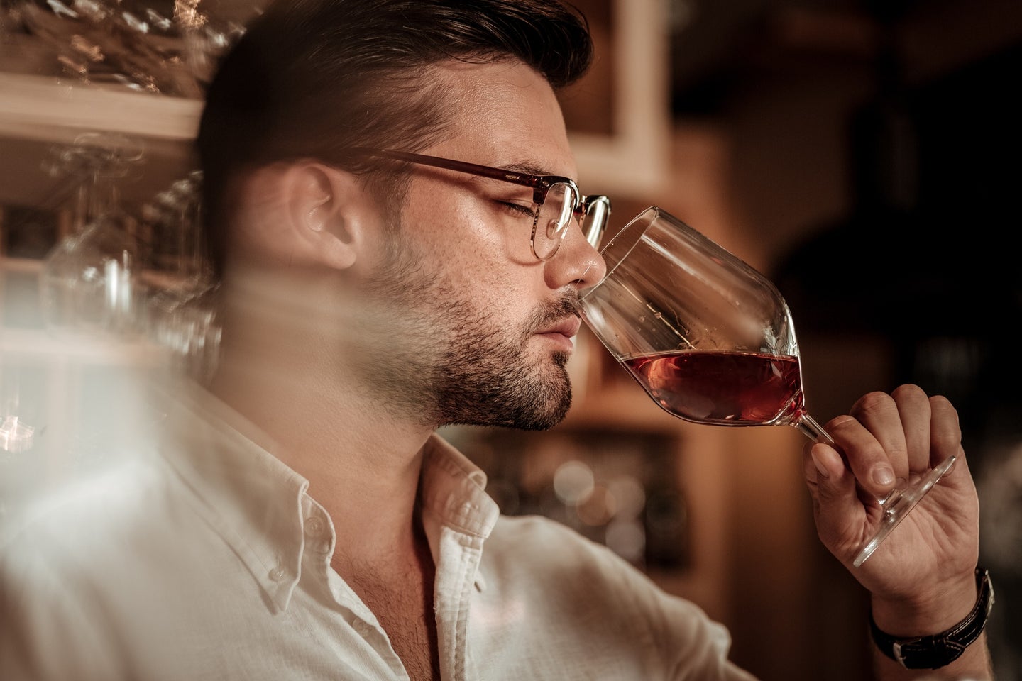 Person with short brown hair and glasses inhaling from a glass of red wine to describe the smell