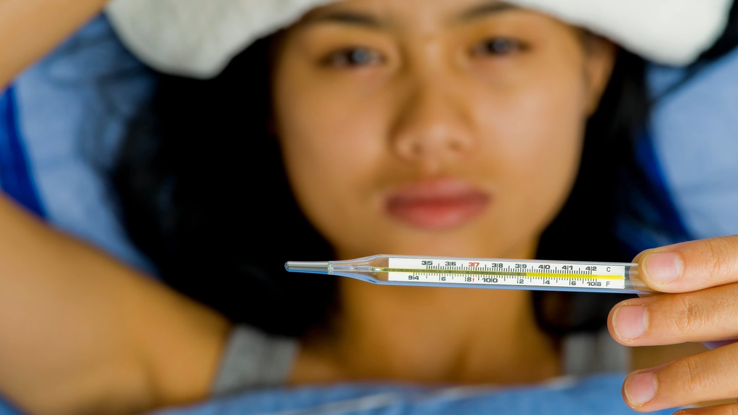 Sick person with tan skin and black hair checking fever on a thermometer