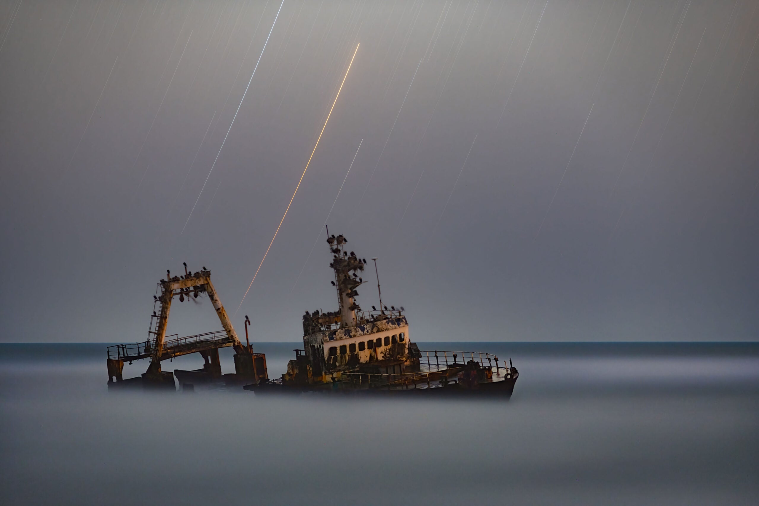 A shipwreck disappears in the fog under stars