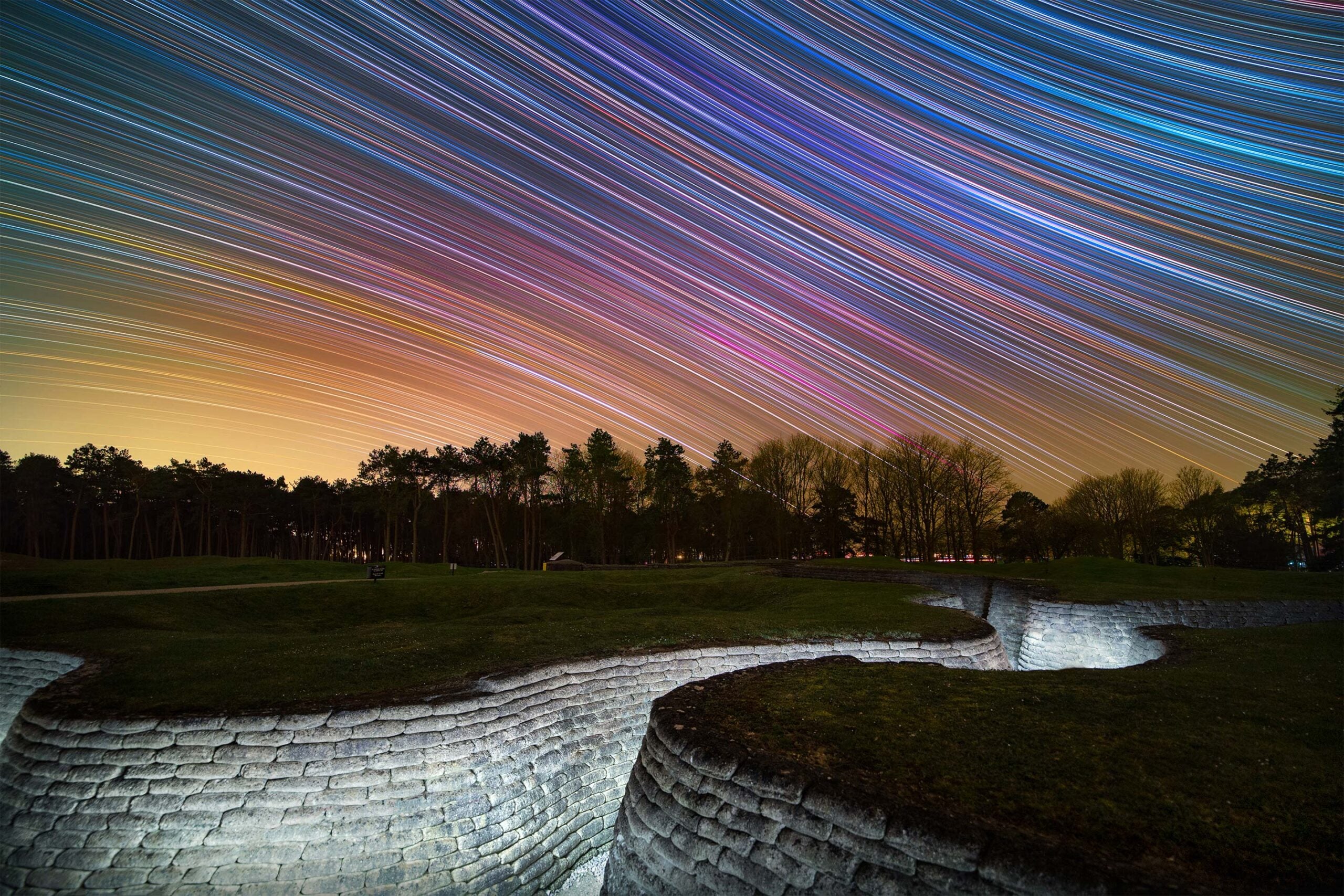 Rainbow-colored star trails over a stone wall