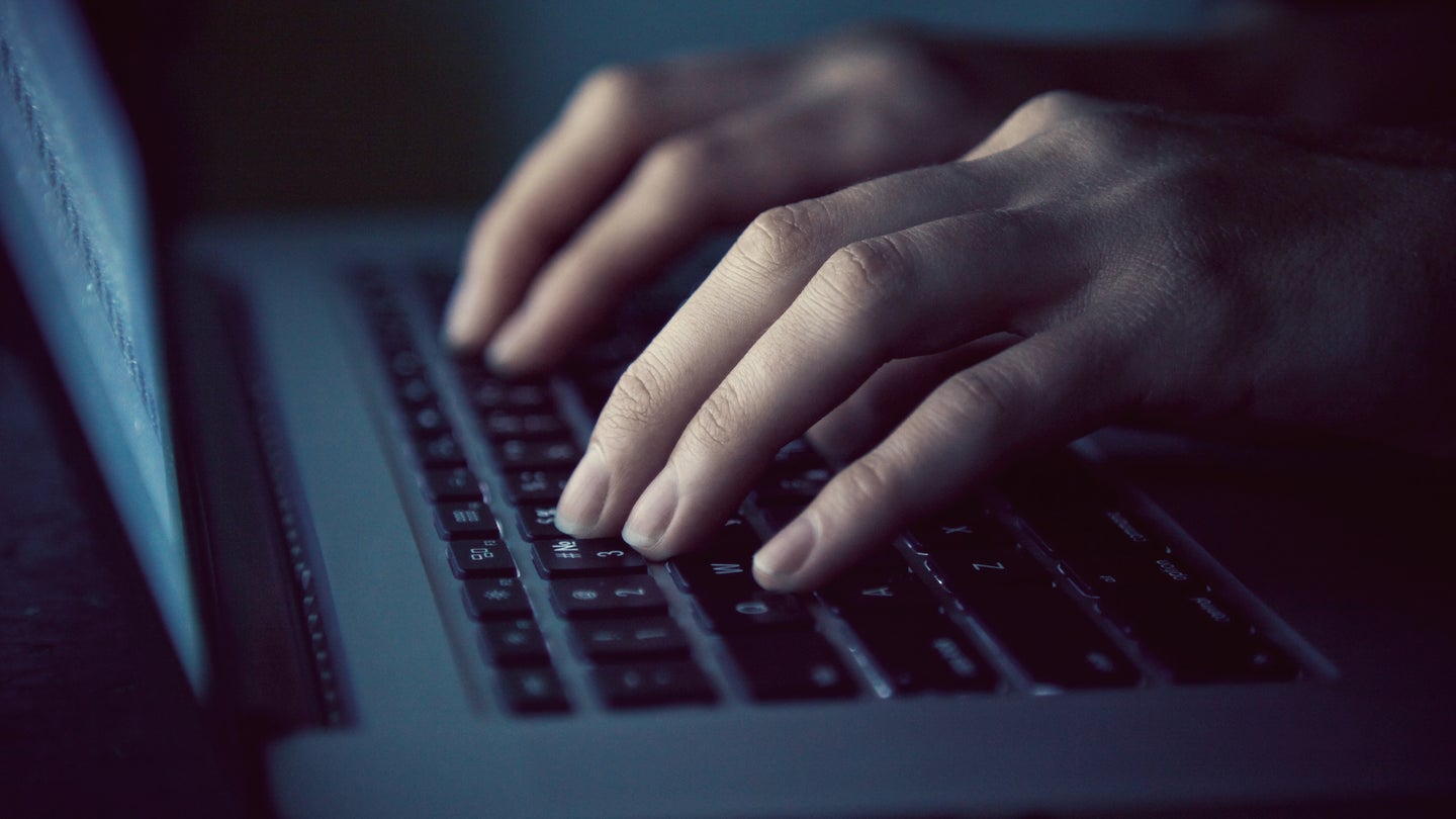 Hands typing on laptop in dark room
