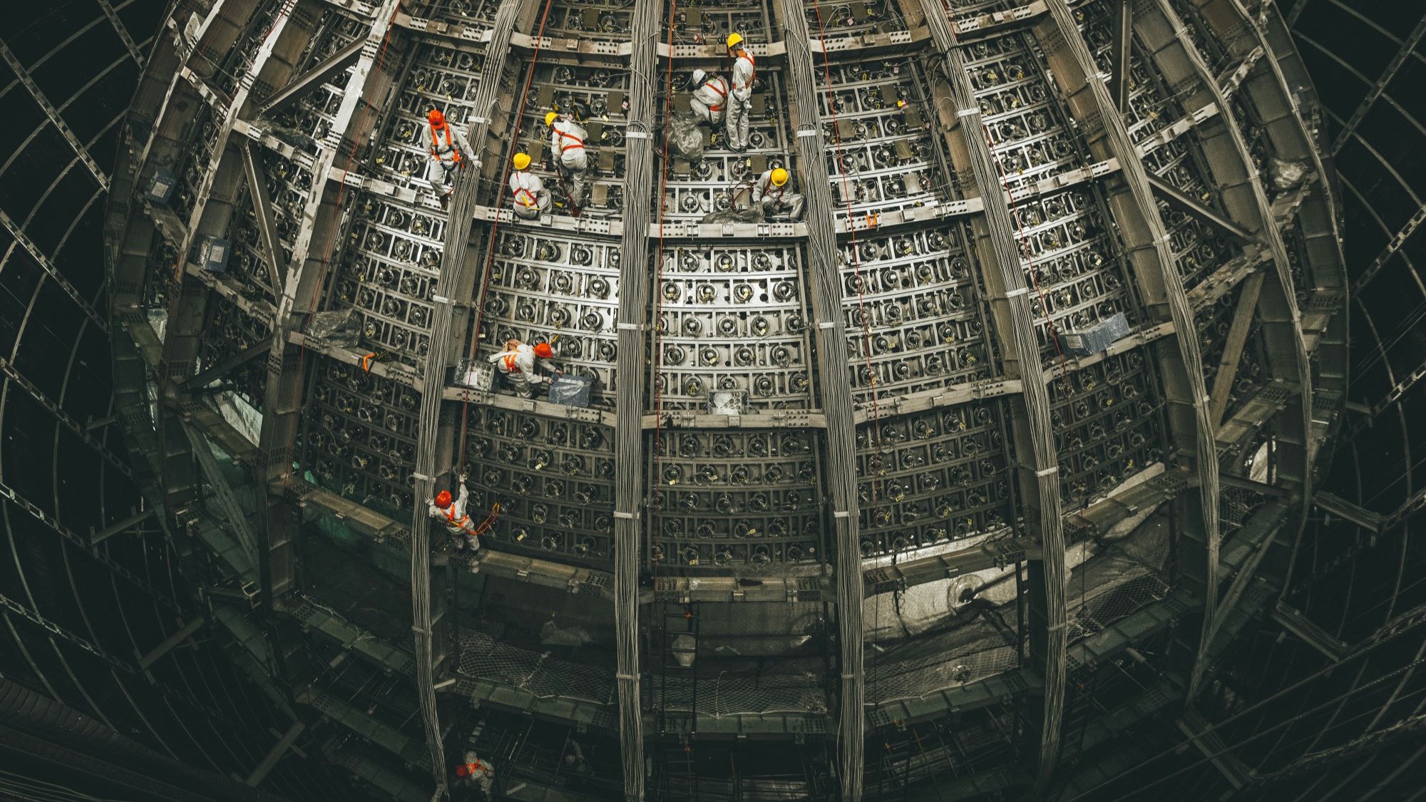 A metal sphere under construction as workers climb over it.
