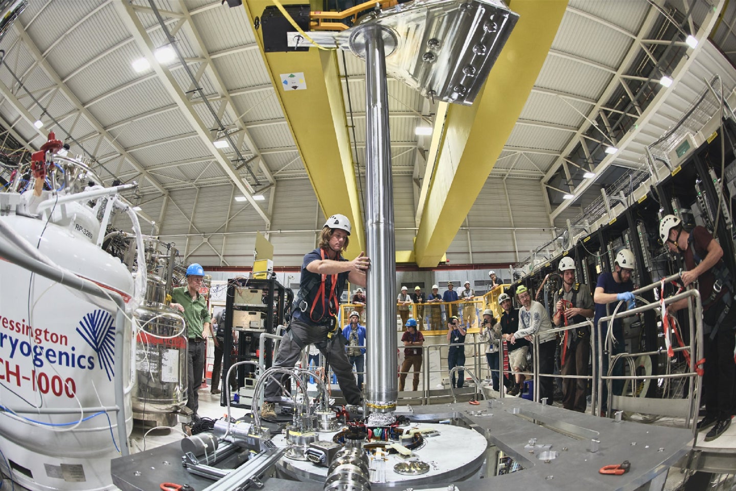 CERN scientists in hard hats putting antihydrogen in a vacuum chamber tube to test the effects of gravity on antimatter