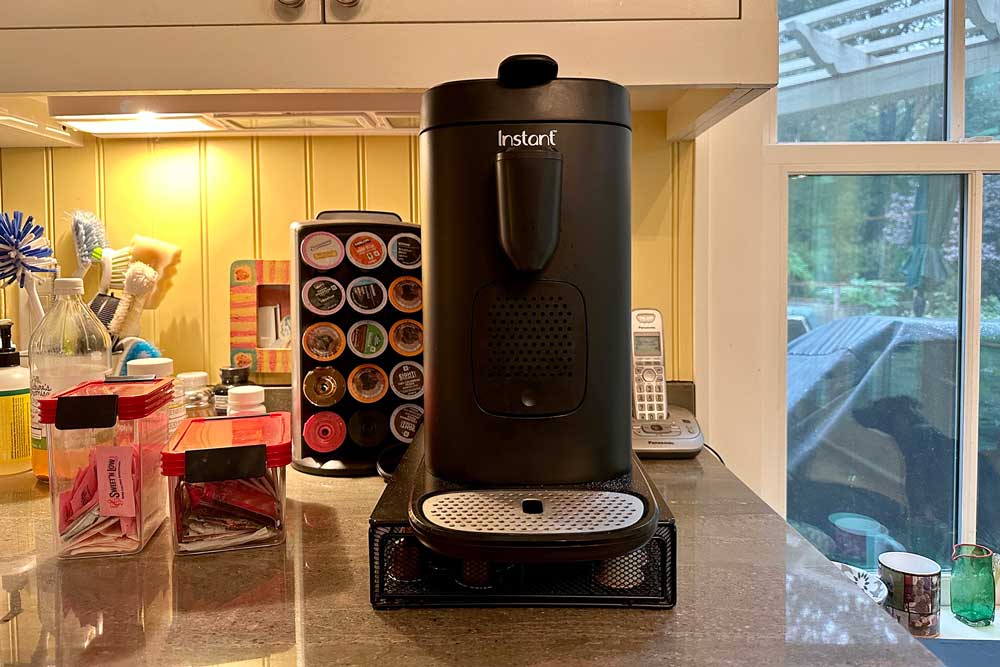 A black Instant Pot pod coffee machine on a counter with Nespresso and Keurig pods