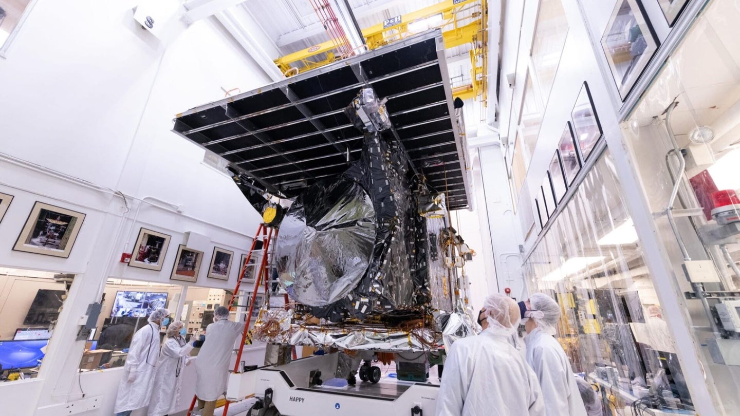 A spacecraft in a white room as technicians wearing cleanroom suits look on.