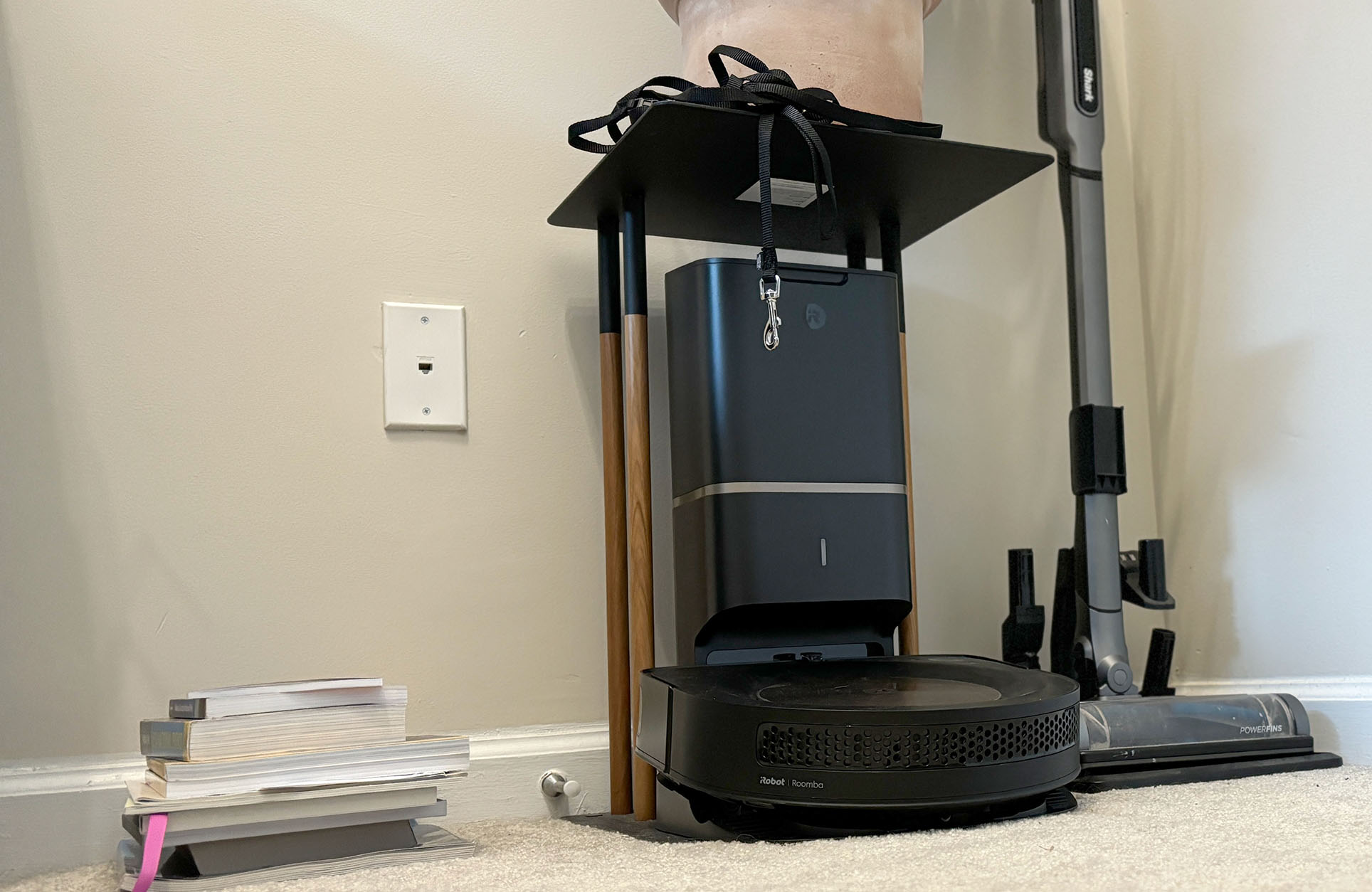 Black iRobot Roombas s9+ on its dock under a plant stand in a corner