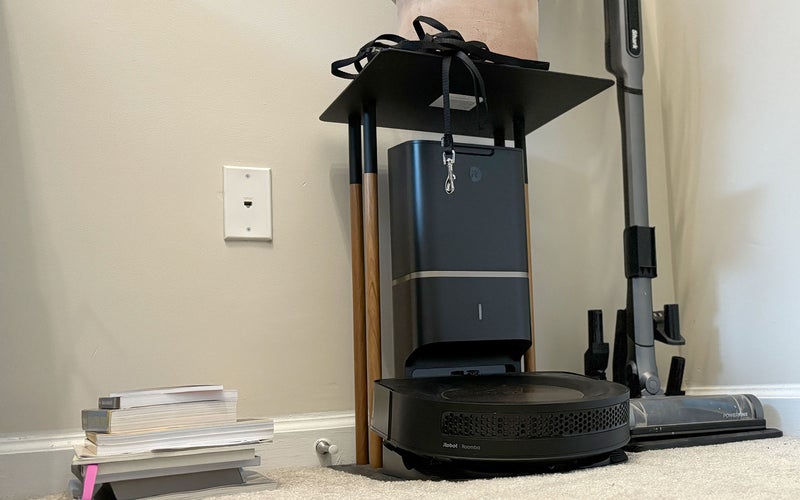 Black iRobot Roombas s9+ on its dock under a plant stand in a corner