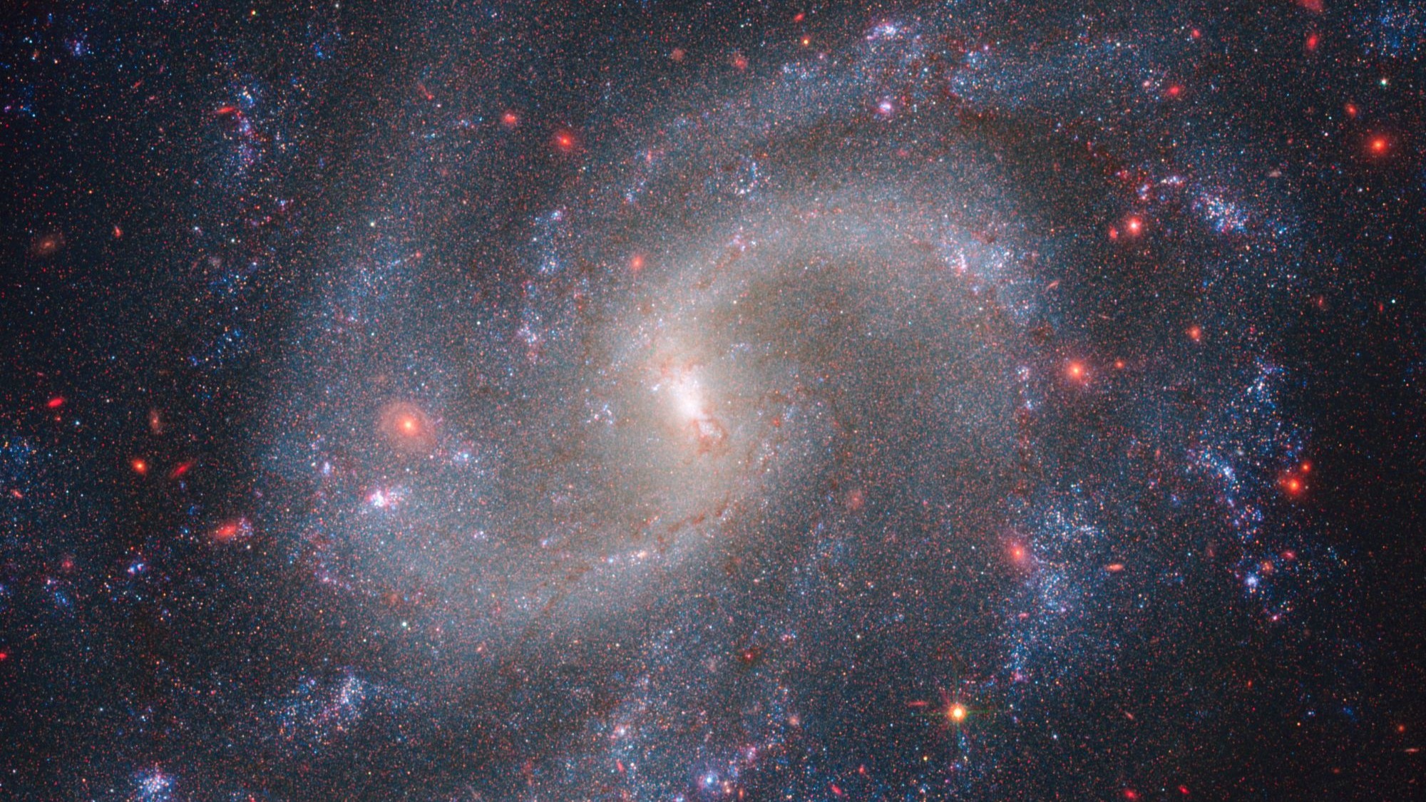 A purplish spiral galaxy with red and yellow space objects.