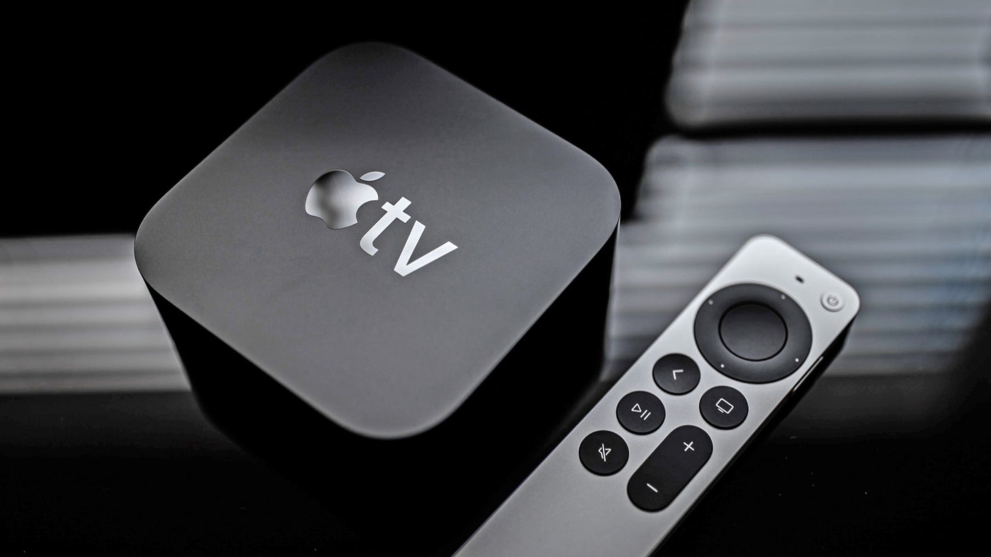 An Apple TV 4K box with a remote next to it, both on a black reflective surface.