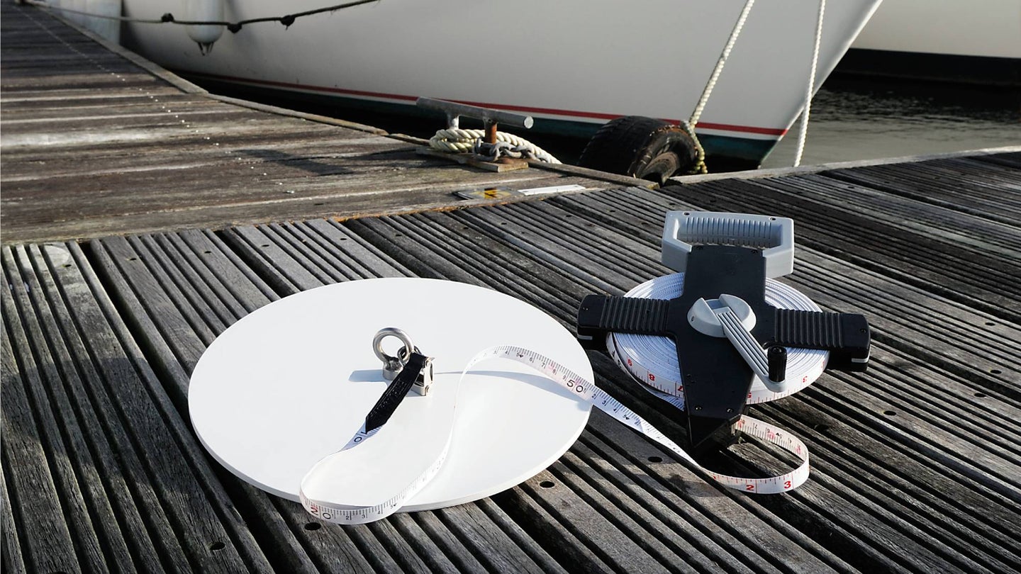 A Secchi Disk and a measuring tape on a gray wooden floating pier next to a moored boat.