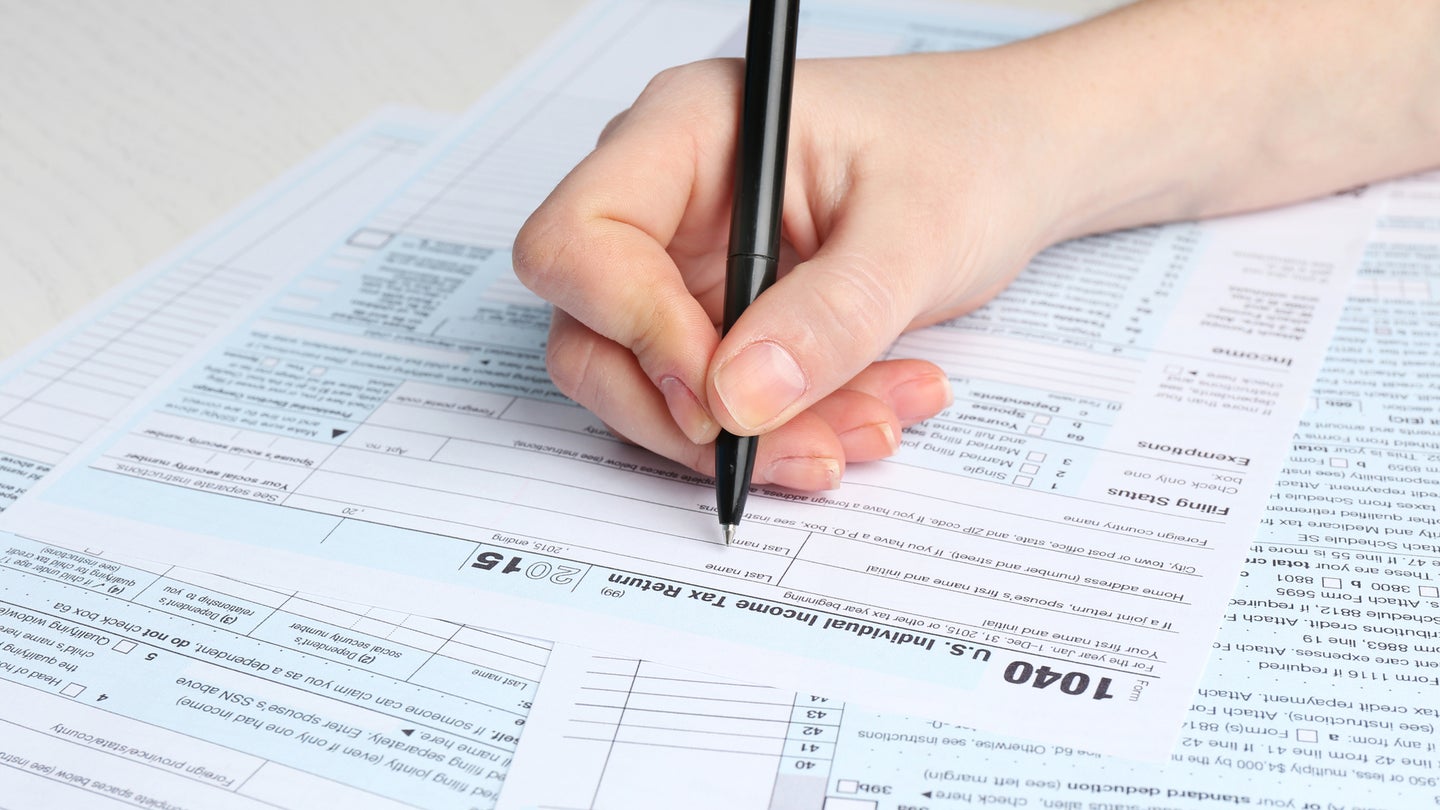 A hand holding a black pen and filling in the 1040 Individual Income Tax Return Form