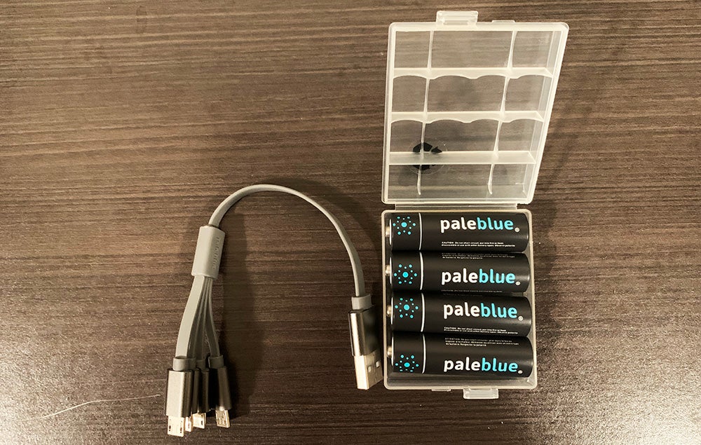 Four AA rechargeable batteries made by Pale Blue in a plastic case, next to a four-pronged USB charger.