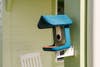 A blue Bird Buddy bird feeder mounted to a post on a front porch.