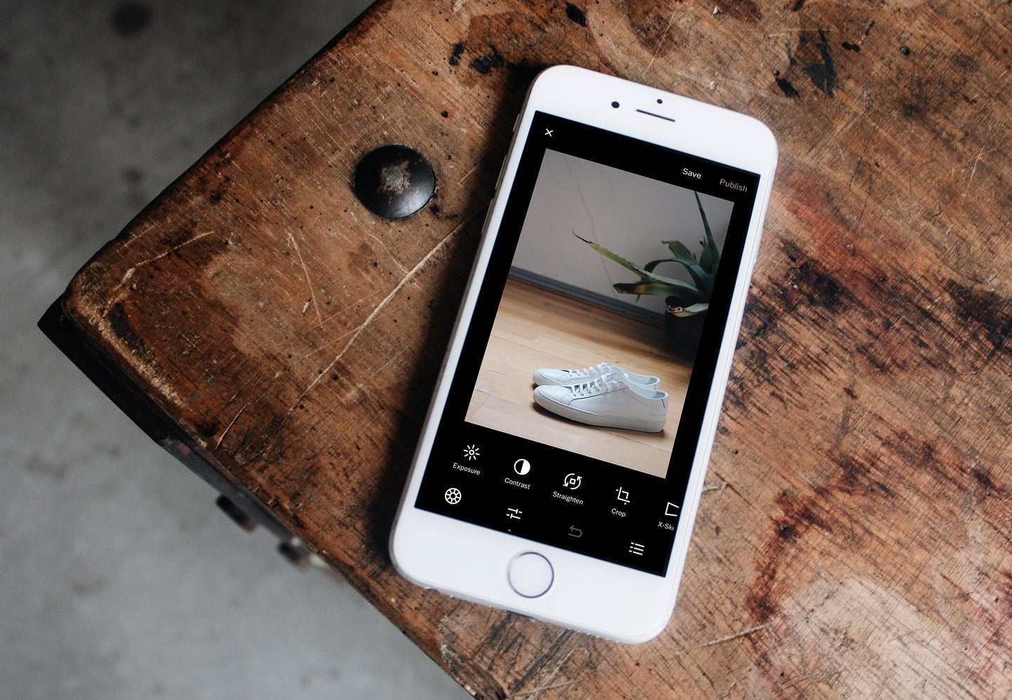 An iPhone on a wooden table, with the Photos app open to an image of shoes that someone is about to edit.