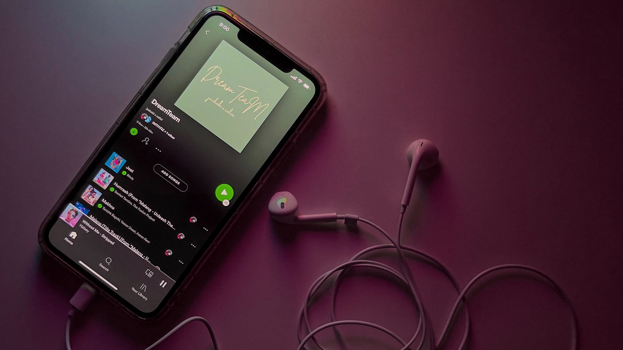 An iPhone connected to white, wired earbuds showing a Spotify playlist on the screen.