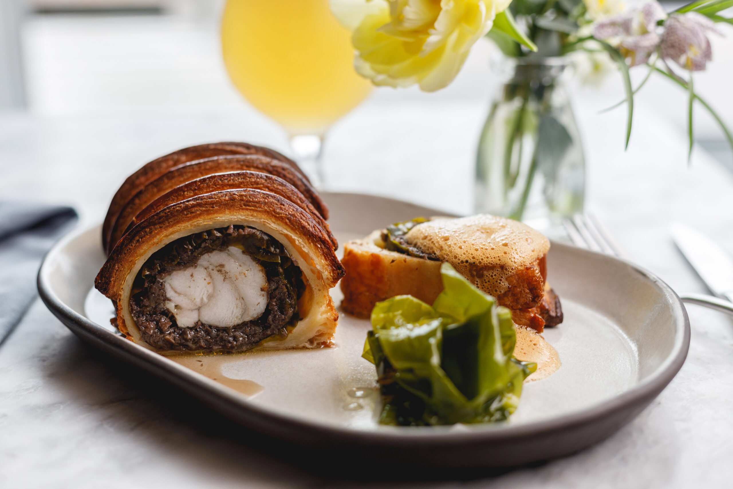 Monkfish Wellington wrapped in a puff pastry with pickled green sugar kelp on the side on a white plate.