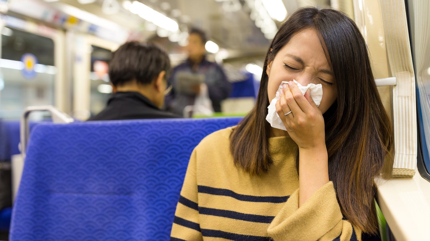 Woman sneezing into tissue on train