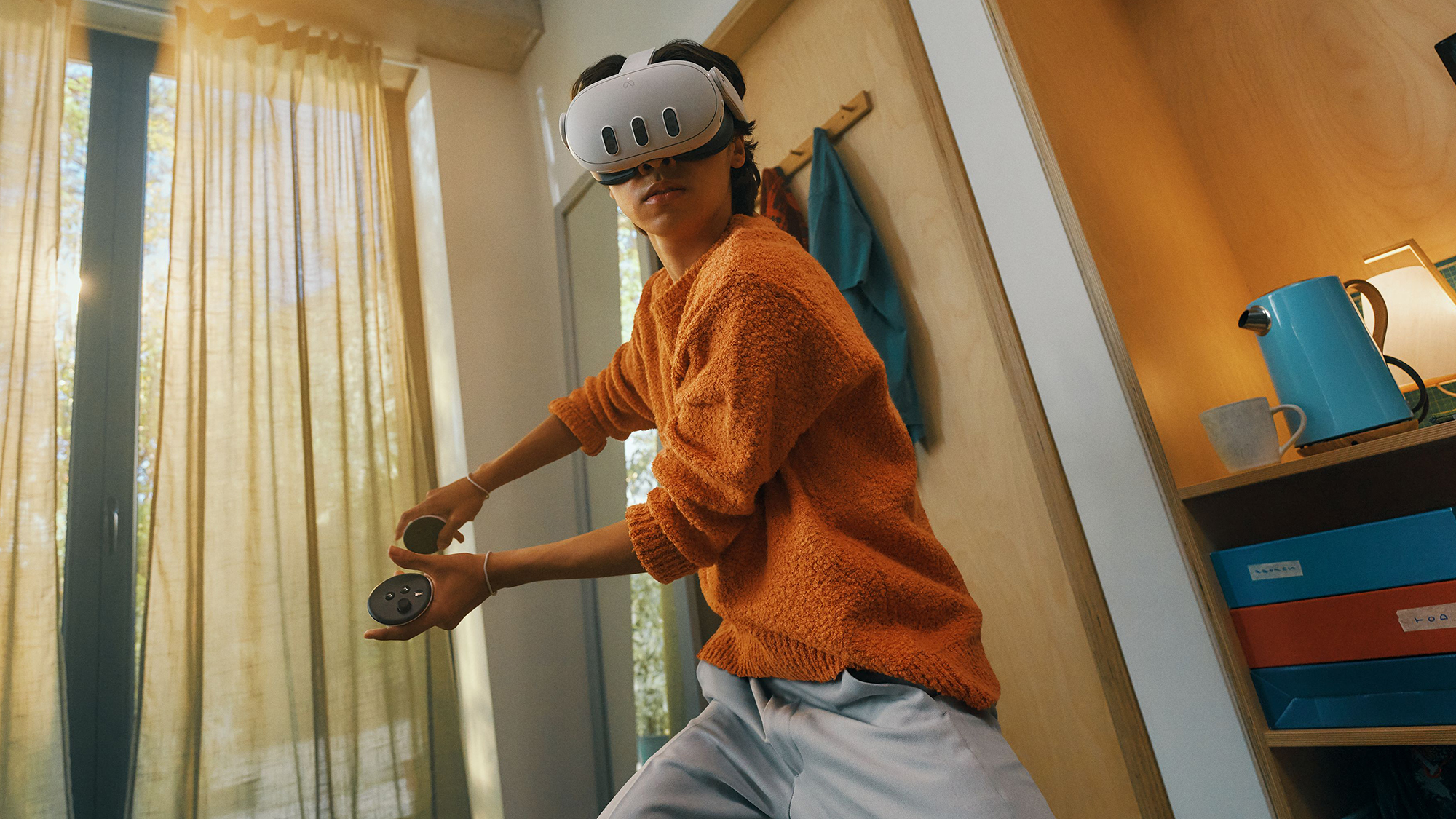 A person wearing an orange sweater and gray pants striking an active pose in a room while wearing and using a Meta Quest 3 headset.