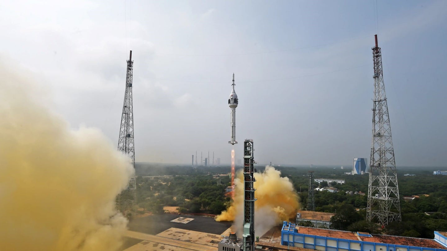 An ISRO rocket launches amid a brownish plume of exhaust.