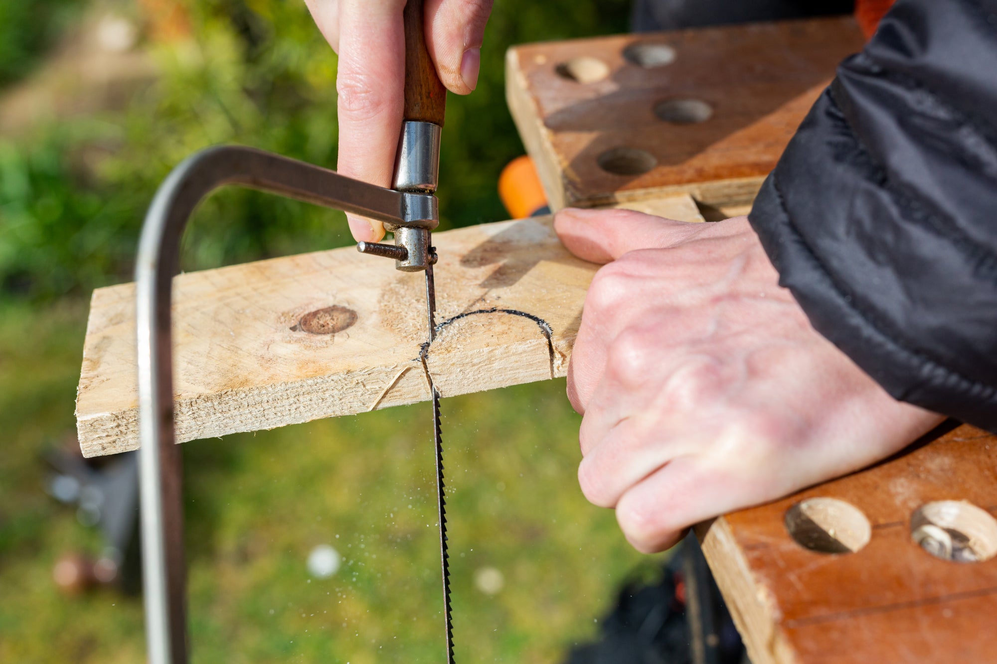 A person using a coping saw to cut a semicircle out of a small piece of wood.