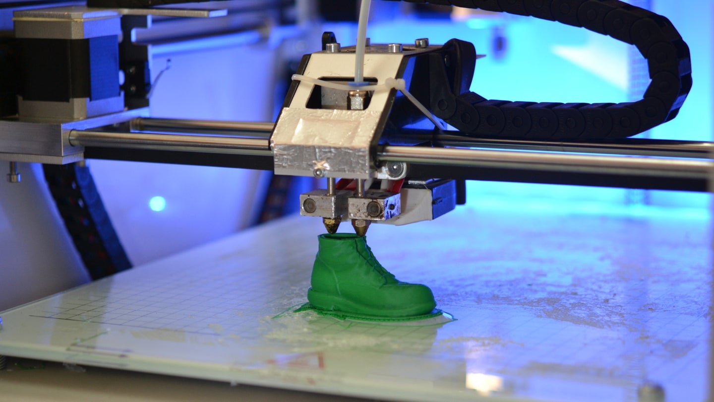 A 3D printer printing a green plastic shoe.