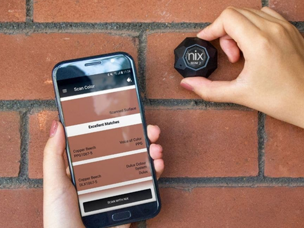A person using a color-matching sensor on a brick wall while holding their phone