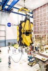 The gold mirrors of the JWST hang in a large room at NASA Goddard with groups of scientists working below.