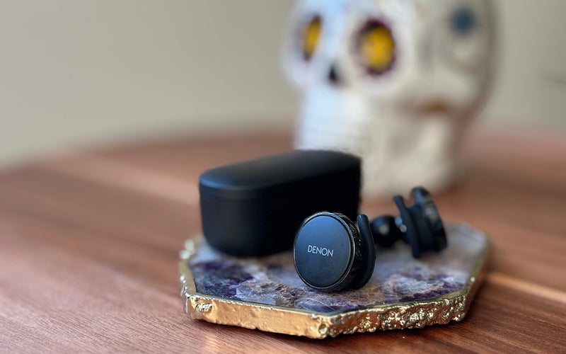Black matte Denon PerL Pro True Wireless earbuds on an amethyst coaster in front of a colorful sugar skull candle