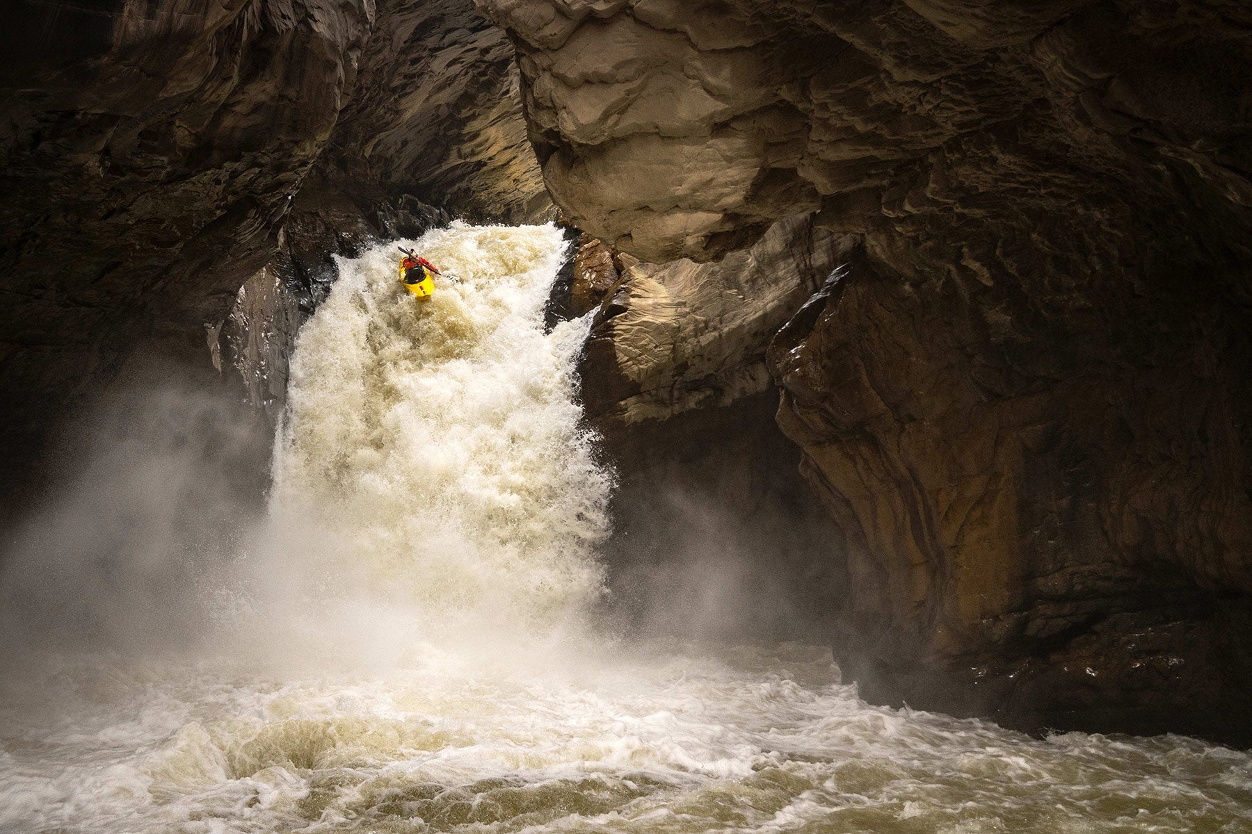 A kayaker is paddling down a fiercely flowing waterfall into a deep canyon.